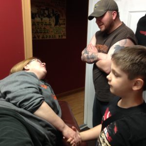 Melissa Marshall's nephew holds her hand as she waits to get tattoo. Her brother Gerald Haught chats with her.