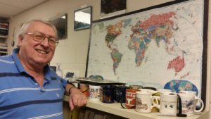 Dale Smith shows world map in his office covered with pins on the 60-plus countries he has visited.