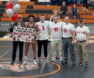 Bowling Green High School wrestler holds 100 wins sign and stands with 4 coaches