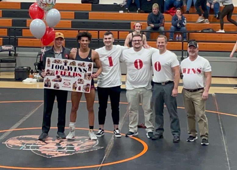 Bowling Green High School wrestler holds 100 wins sign and stands with 4 coaches