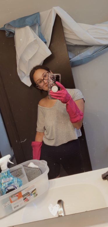 Woman with cleaning supplies takes selfie with camera