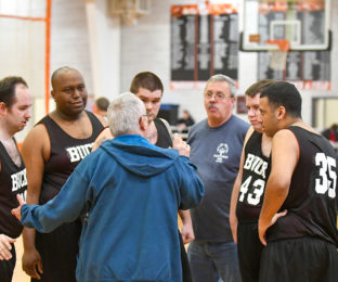 Coach talks to 4 Special Olympics Basketball Team members and volunteer