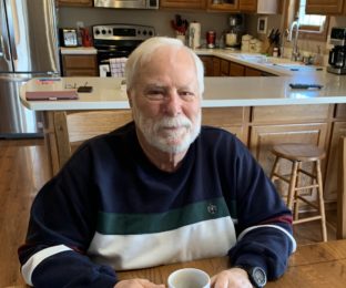 man sits at table holding coffee mug
