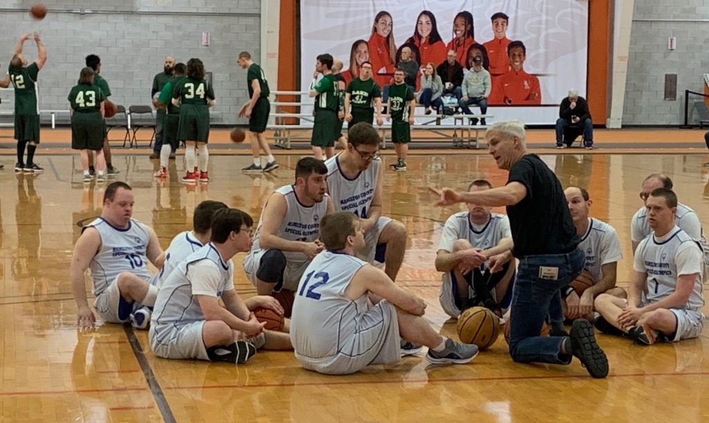 Men basketball players seated on floor as man talks and points