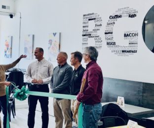woman and four men hold green ribbon for ribbon cutting ceremony