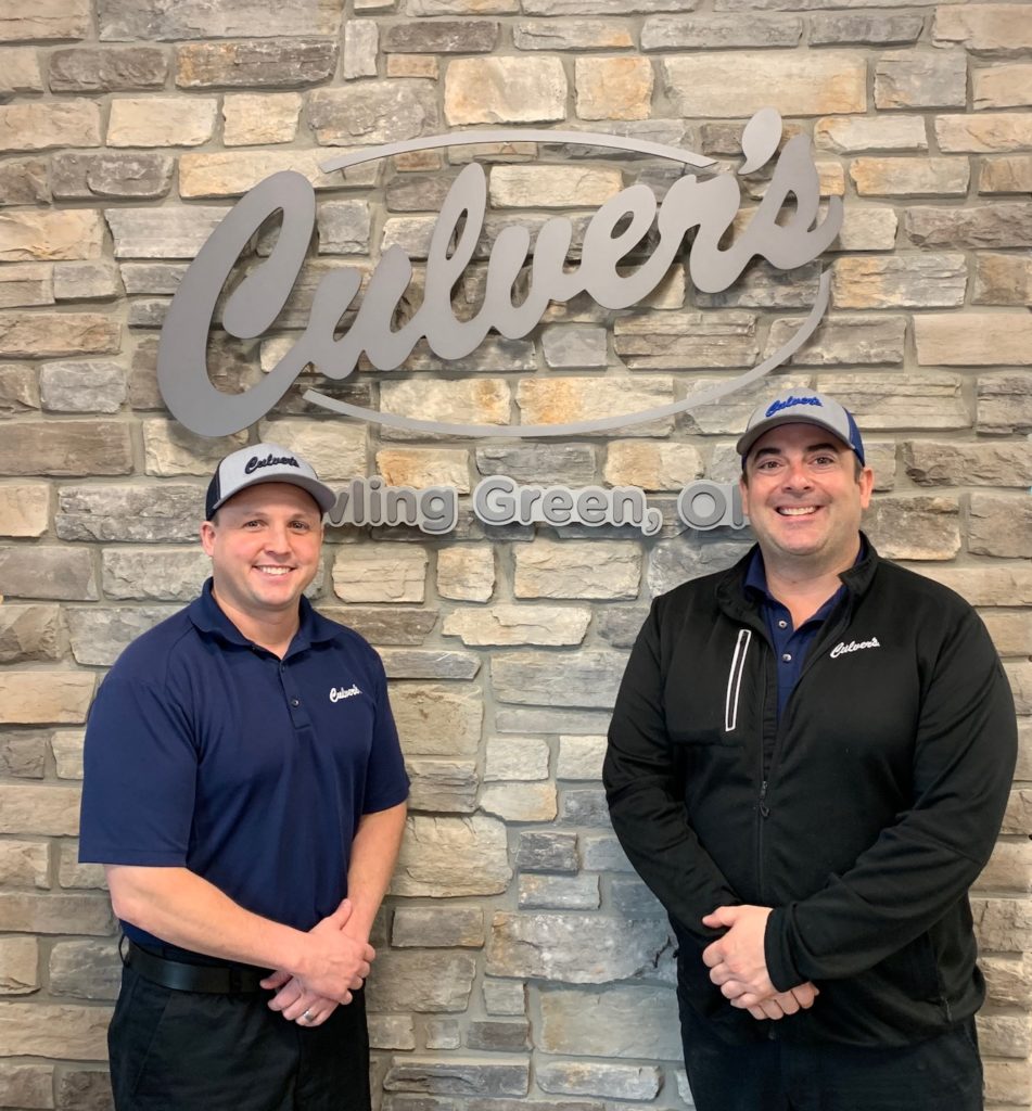 Two men stand near Culver's lettering on brick wall