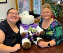 Two women with stuffed toy black and white cow between them