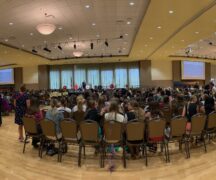 Room full of girls state members seated watching program on stage