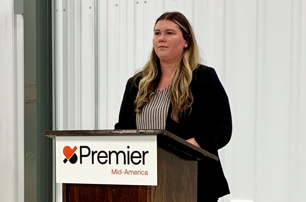 Woman at podium with sign Premier Mid-america