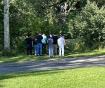 backs of group of boys as they stand in wooded area.