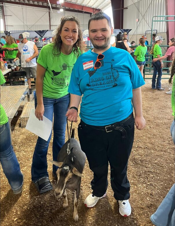 Woman stands next to man who is holding a goat on a leash.