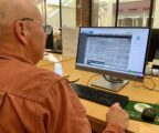 Computer screen is seen over the shoulder of man looking at a historical newspaper website.