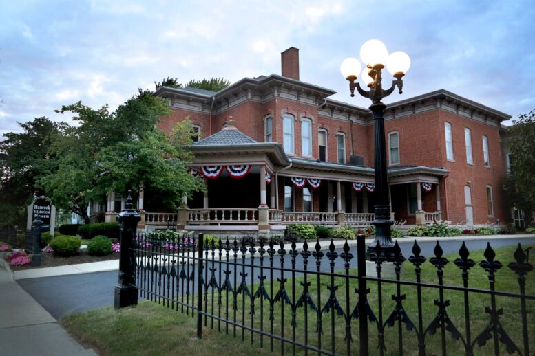 Picture featuring a large historic brick building, which is a museum, a blue sky, and a wrought iron fence.