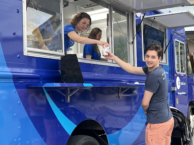 A person in a blue food-type-truck gives a drink in a cup to a man standing outside of the truck