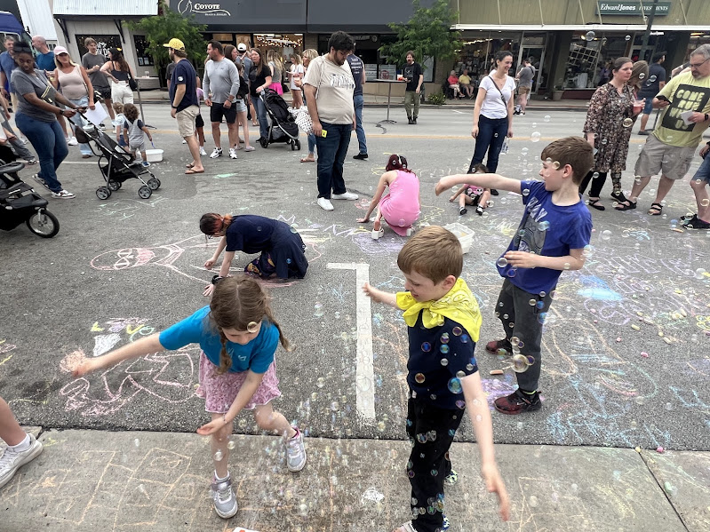 children dance through bubbles on a street covered in sidewalk chalk