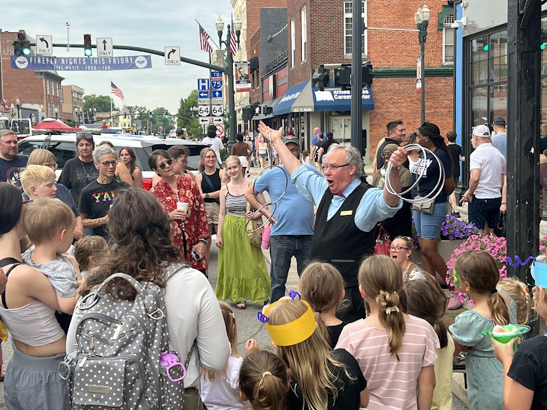 a magician holds two sets of three rings and performs in the middle of a crowd