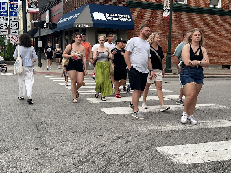 pedestrians cross the street in front of the Armed Forces Career Center building, which is brick with a blue awning