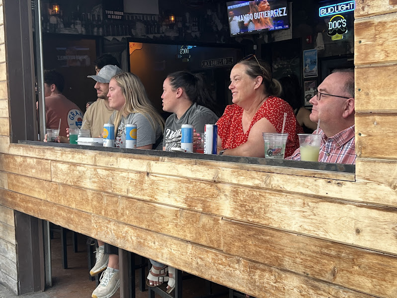 five people sit at a bar with a window out to the sidewalk