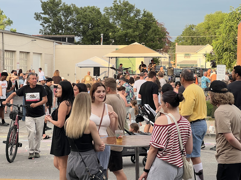 a crowd of people listen to music and drink while some sit and some stand