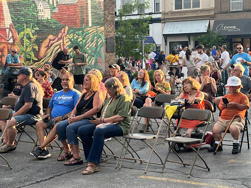 a crowd sits in chairs in a parking lot, listening to music