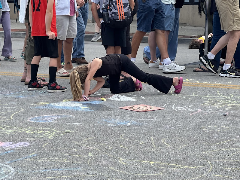 Photo shows young girl in an odd position, focused on coloring the pavement with chalk