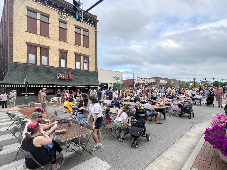 Photo shows people gathered downtown, some standing, some eating at tables that are lined up