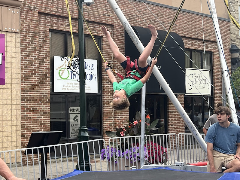A child is jumping on a trampoline in a harness, allowing him to flip upside down.