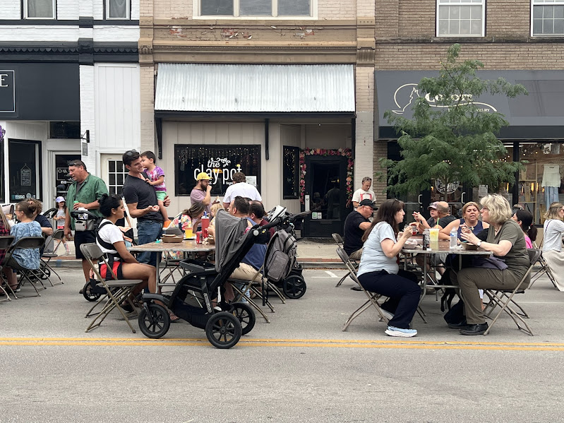 people eat at tables set up in the middle of the street in front of downtown stores