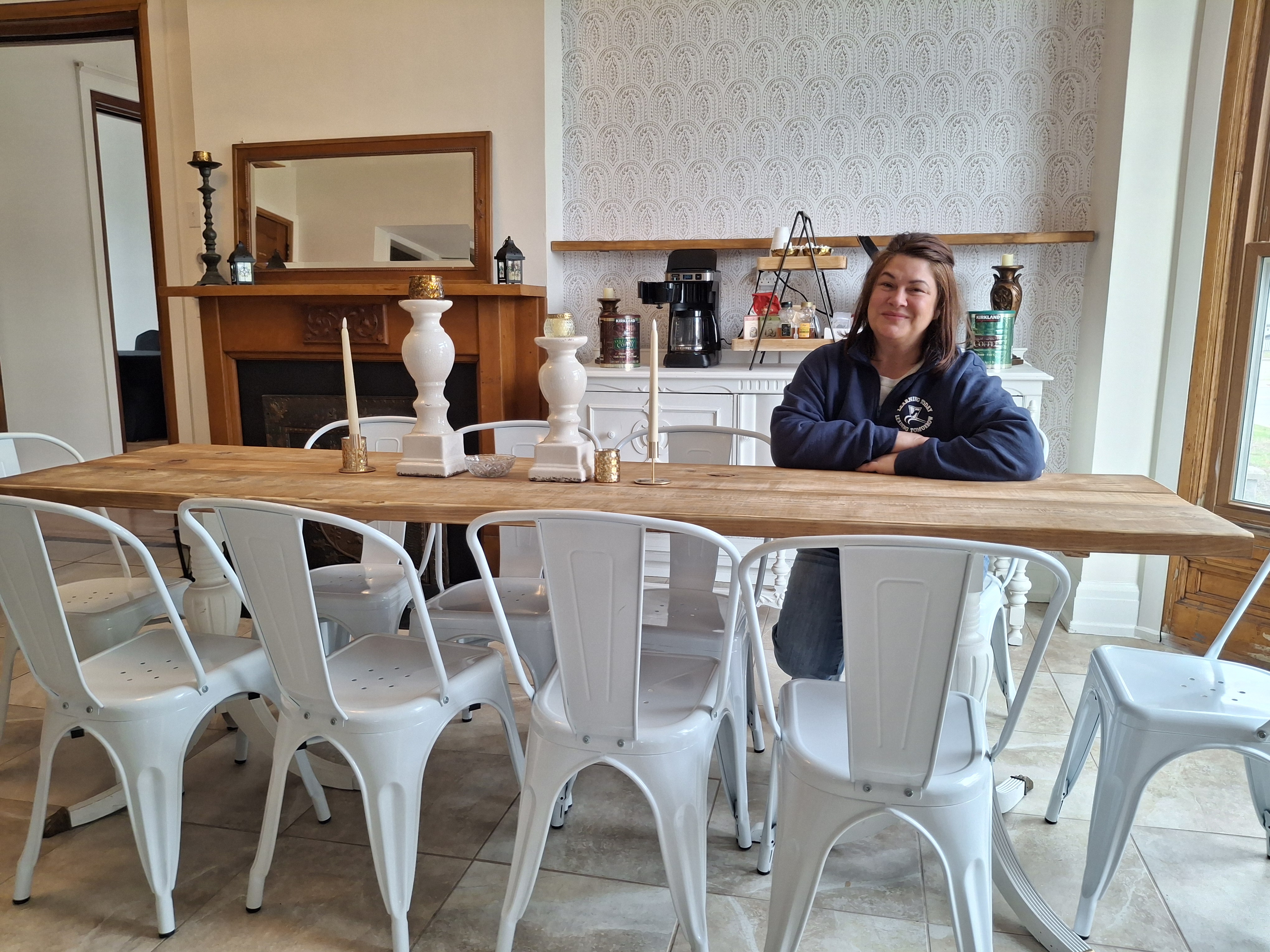 Woman in a blue sweatshirt sitting at a long dining table.