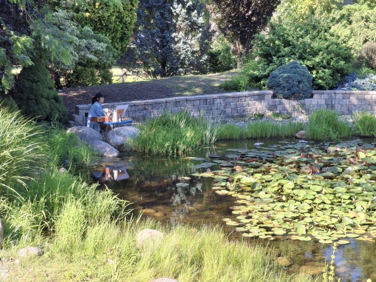 A woman with easel and oil paints next to a waterlily pond.