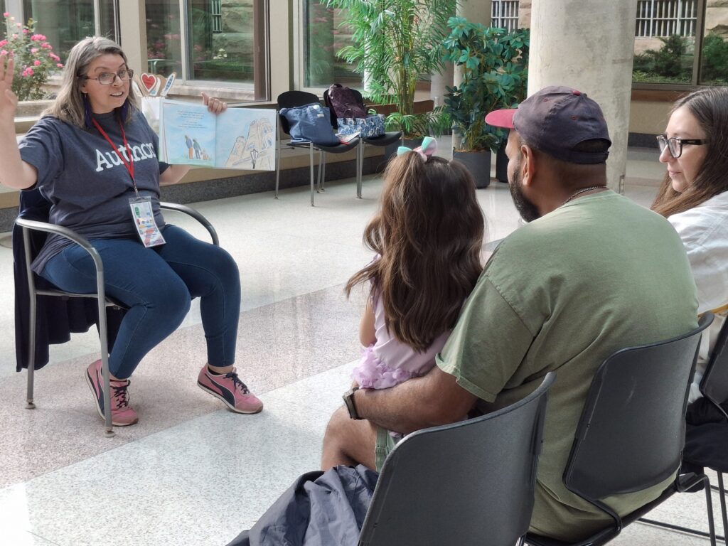 A woman wearing a shirt saying "author" reads to a family from a picture book