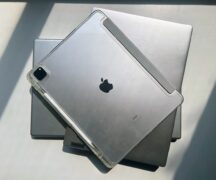 two silver laptops and a silver ipad are stacked on each other, closed