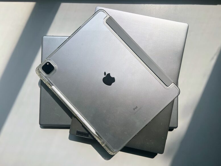 two silver laptops and a silver ipad are stacked on each other, closed