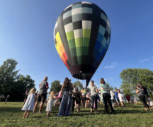around 50 people gather around an inflated hot air balloon that is grounded