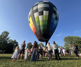 around 50 people gather around an inflated hot air balloon that is grounded