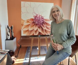Artist Mary Dawson in front of a work in progress of a dahlia.