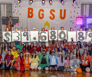 Large group of students dressed in colorful costumes holding up signs with $39680.87.
