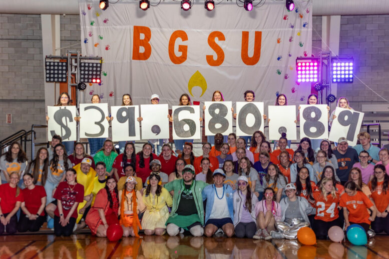 Large group of students dressed in colorful costumes holding up signs with $39680.87.