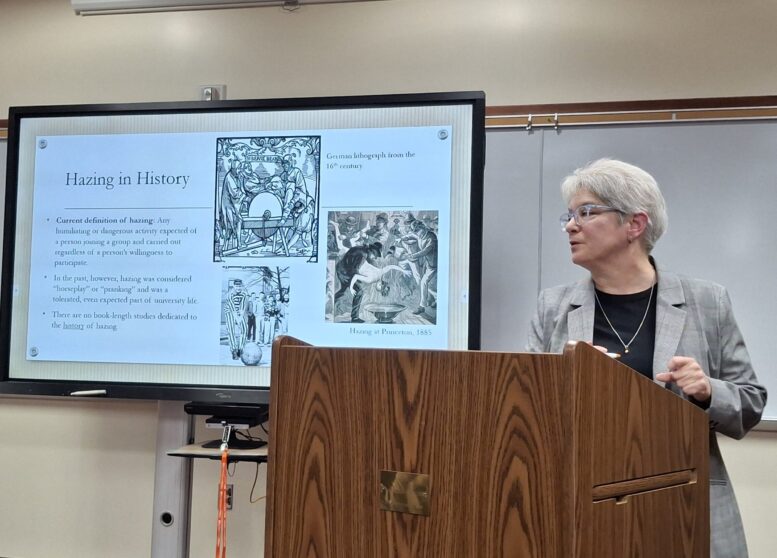 Dr. Rebecca Mancuso in front of a slide describing hazing throughout history