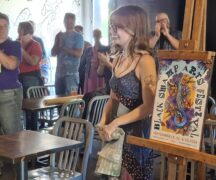 Smiling woman show her work on the new poster for the Black Swamp Arts Festival