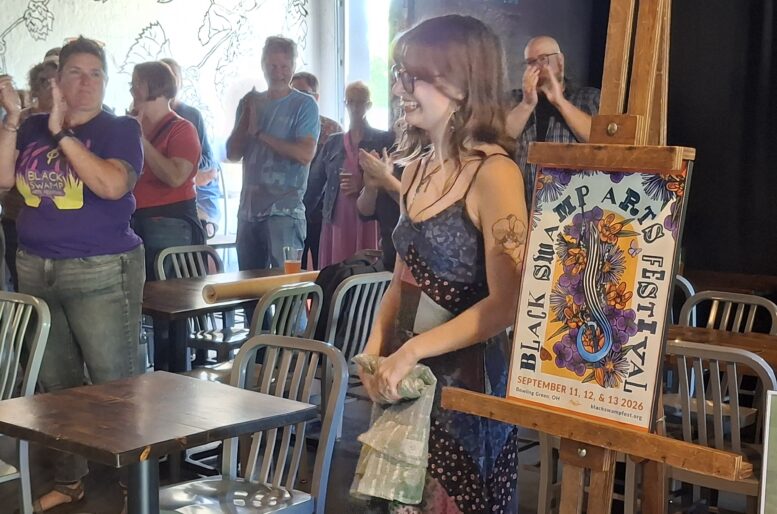 Smiling woman show her work on the new poster for the Black Swamp Arts Festival